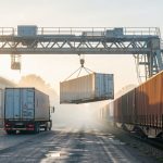 Quelle solution rail-route choisir pour moins dépendre du tout-routier ? Terminal français de transport combiné où un portique transfère une caisse mobile entre un camion et un train de marchandises, dans la lumière matinale.