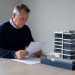 Un homme consultant des documents financiers vierges devant une maquette détaillée d’immeubles de bureaux modernes, dans une ambiance sobre et éditoriale.